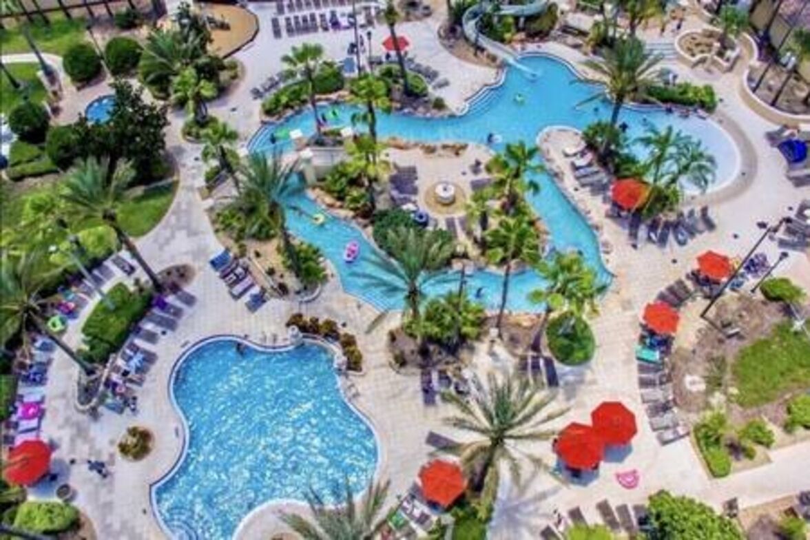 Eine Luftaufnahme eines Resorts mit mehreren Schwimmbecken, Liegestühlen und Palmen.