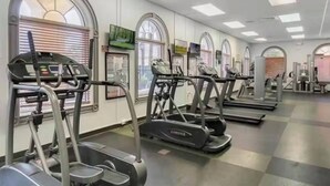 Ein Fitnessstudio mit mehreren Laufbändern und Crosstrainern, großen Fenstern mit Jalousien und einem klaren, modernen Design.
