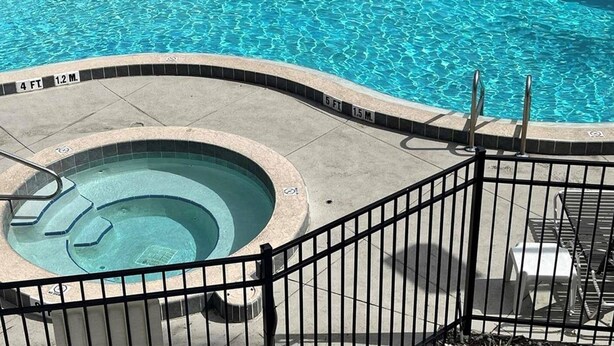 Ein Schwimmbecken mit Whirlpool, umgeben von einem schwarzen Metallzaun.