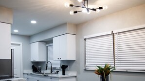Una cocina moderna con armarios blancos, un comedor con mesa negra y una lámpara colgante.