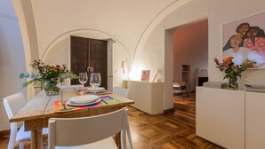 Un coin repas avec une table en bois, des chaises blanches et une petite cuisine en arrière-plan.