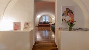 Un couloir doté d’un plancher en bois, de murs blancs et d’un plafond voûté. Des œuvres d’art encadrées ornent les murs, et un vase rempli de fleurs est posé sur une table.