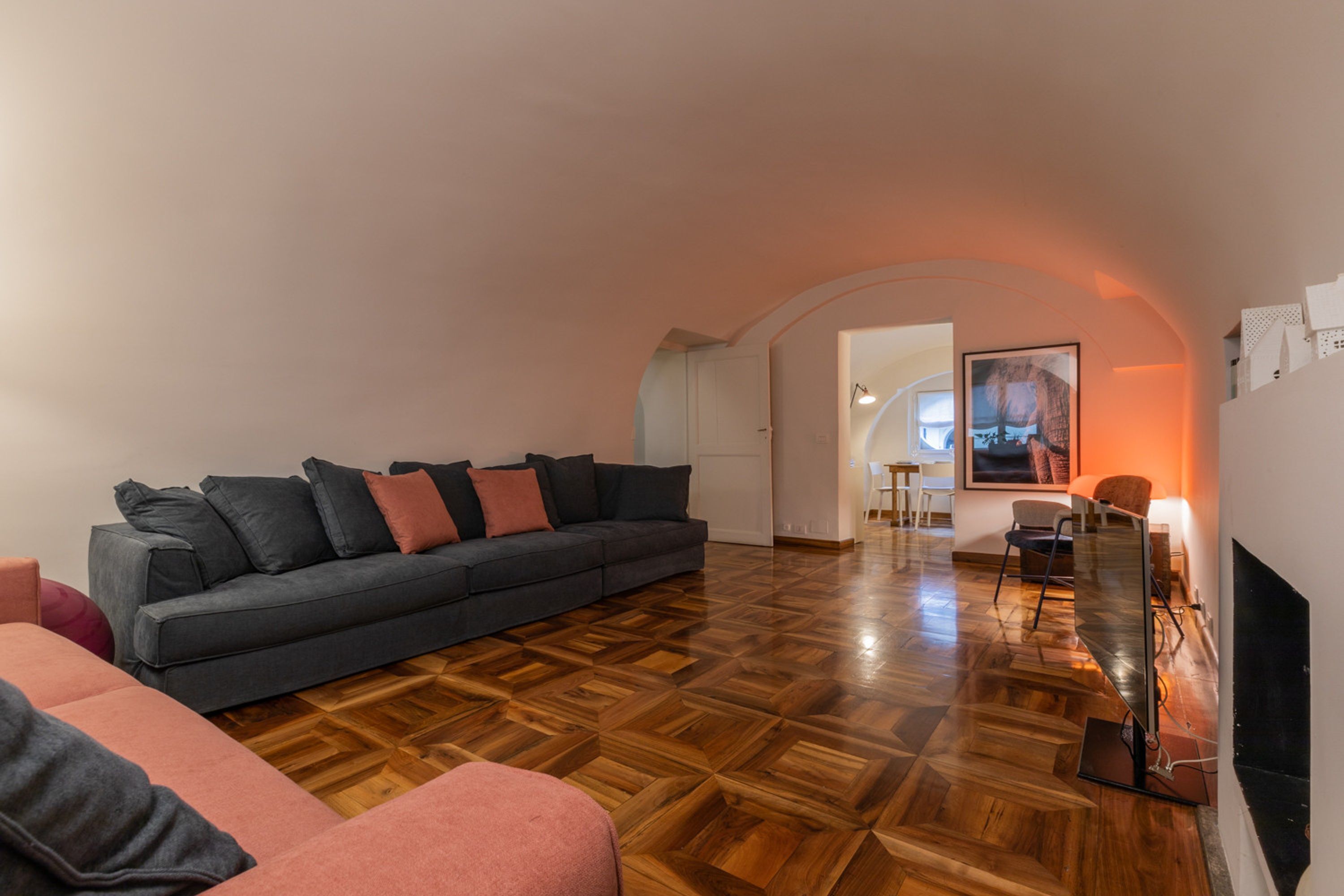 Una sala de estar moderna con un sofá gris oscuro, un sillón rosa y un suelo de parqué de madera.