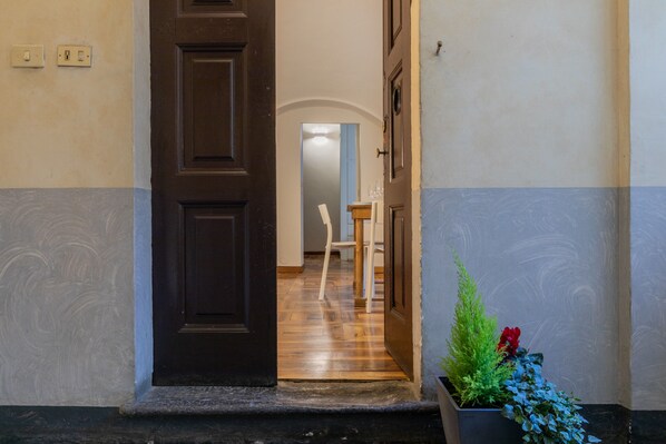 Un pasillo con una puerta de madera, una planta en maceta con flores rojas y una silla blanca.