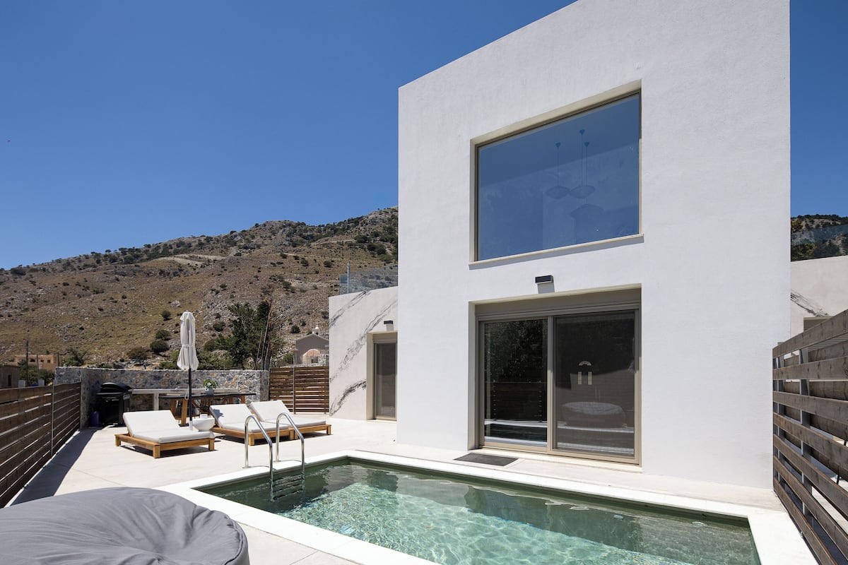 A modern outdoor pool area with clear water, lounge chairs, and a view of a hilly landscape.