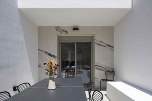 A modern outdoor dining area with a marble wall, a table with chairs, and a view into a covered patio. - Imbros Villas – Holiways Collection (Sfakia)