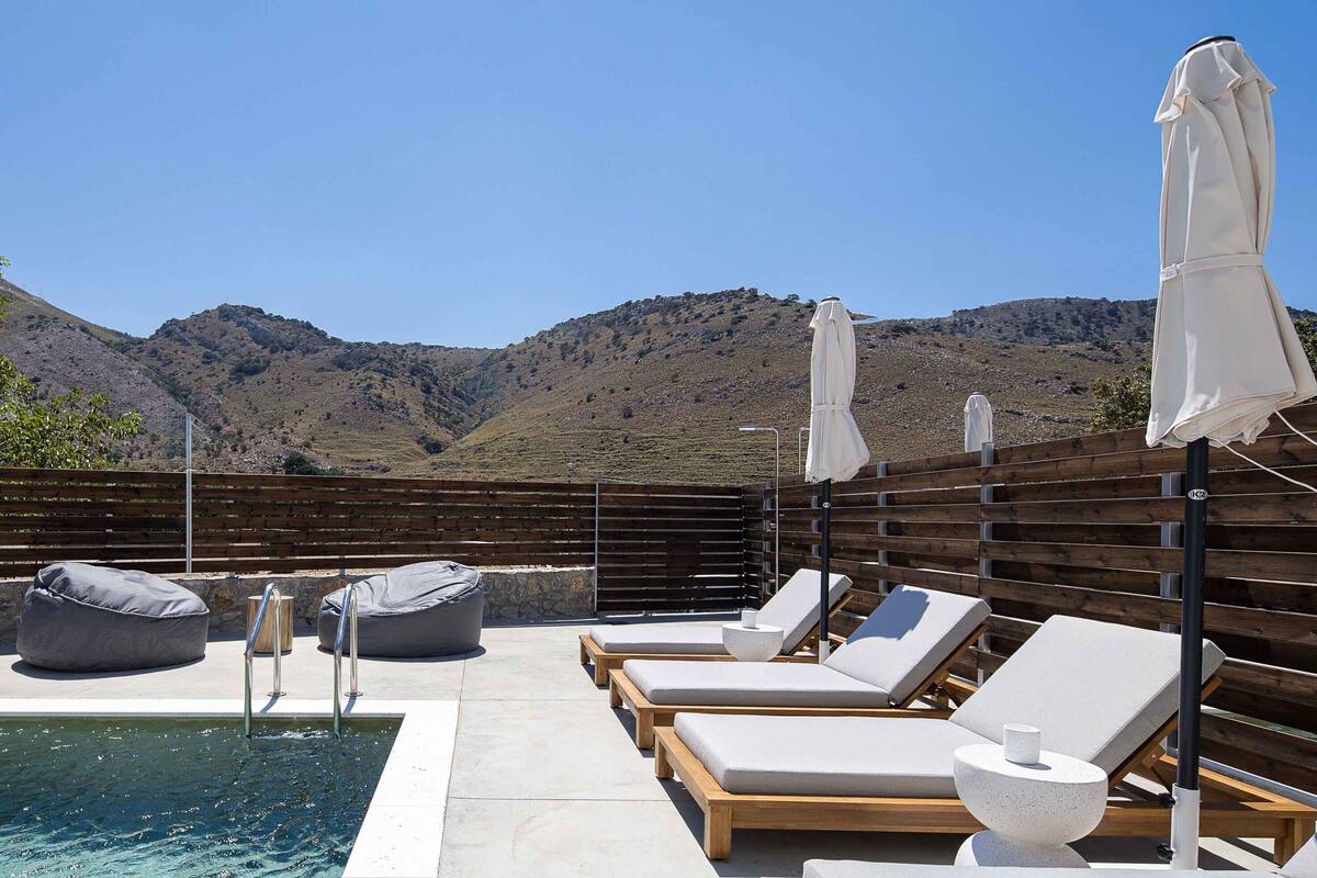 A poolside area with lounge chairs, bean bags, and umbrellas, overlooking a mountainous landscape.