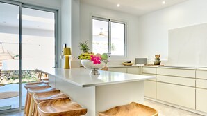 Cozinha moderna com ilha central, banquetas de madeira e uma tigela com frutas e flores.