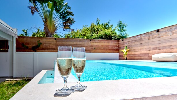 Piscina com dois copos de champanhe na borda, cercada por um muro de madeira e vegetação.