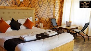 A hotel room with a large bed, a wooden headboard, a wooden herringbone-patterned wall, a small table with a chair, and a kettle on the nightstand. - The Lake View Resort (Sangla)