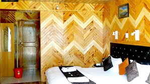 A hotel room with a wooden herringbone wall pattern, a bed with white bedding and multiple pillows, a black headboard, and a red bucket on the floor. - The Lake View Resort (Sangla)