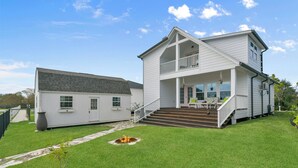 Ein zweistöckiges Haus mit einer Veranda, einem Feuerkorb im Garten und einer Treppe, die zum zweiten Stock führt.