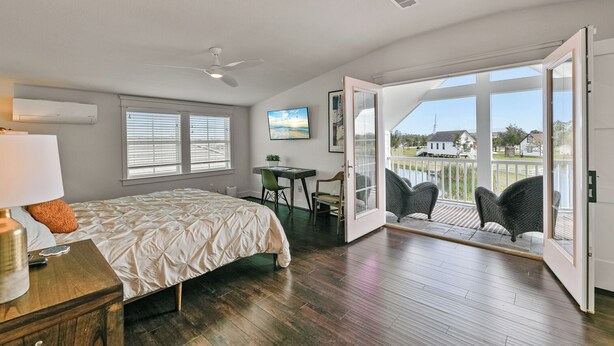 Ein Schlafzimmer mit Bett, Schreibtisch, Stuhl und einem Balkon mit Korbstühlen.