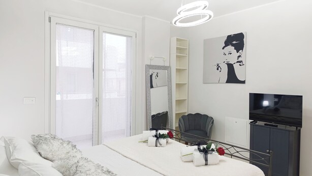 Une chambre moderne avec un lit, une chaise, un téléviseur et un grand miroir.