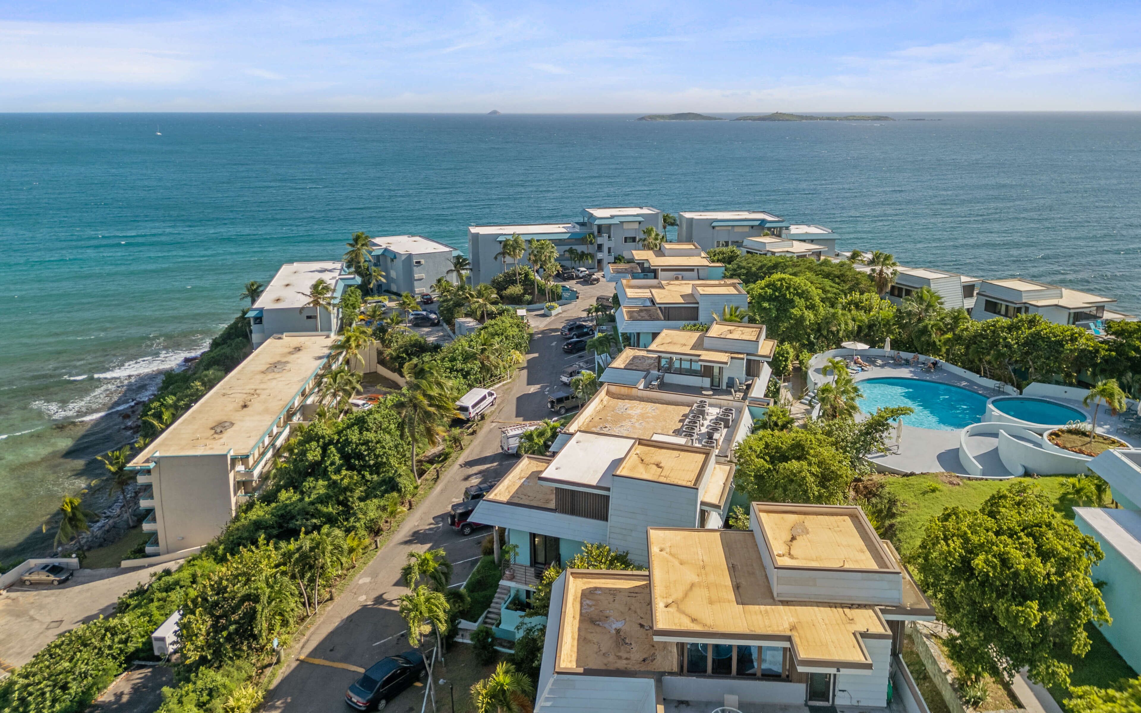 An aerial view of a coastal resort with multiple buildings, a swimming pool, and a view of the ocean.