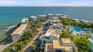 An aerial view of a coastal resort with multiple buildings, a swimming pool, and a view of the ocean.
