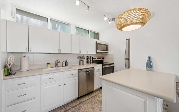 A modern kitchen with white cabinets, a built-in microwave, stainless steel appliances, and a hanging light fixture. - Steve's Seaside Condo-2 Bedrooms-3 Beautiful Pools- Regatta Point Villas (St Thomas)