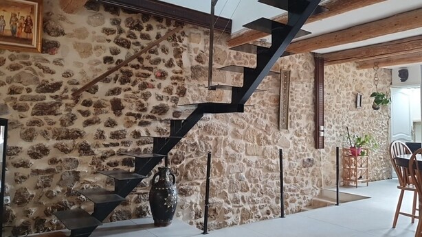 A stone wall with a black staircase, a large vase, and a dining area with chairs and a table. - Old restored village house with terrace (Jouques)