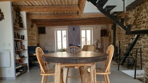 A rustic dining area with a round wooden table and four chairs, surrounded by stone walls and a staircase. - Old restored village house with terrace (Jouques)