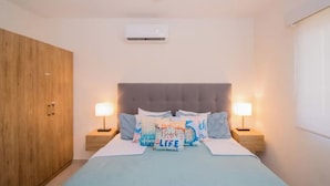 Ein Schlafzimmer mit einem Bett, zwei Nachttischen mit Lampen, einem Kleiderschrank und einer Klimaanlage an der Wand.