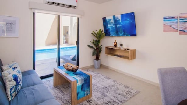 Ein Wohnzimmer mit einer Couch, einem Couchtisch, einer Pflanze und Blick auf den Pool durch eine Glastür.