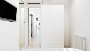 Une chambre moderne et minimaliste, avec un lit, un téléviseur fixé au mur et un radiateur blanc.