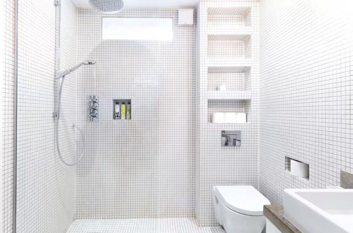 A modern bathroom with a shower, toilet, and built-in shelves.