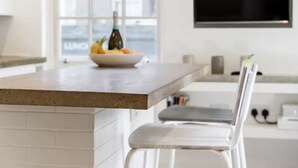 Une cuisine moderne dotée d’un coin bar, de meubles blancs, d’une grande fenêtre et d’un téléviseur à écran plat fixé au mur.