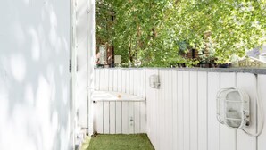 Une clôture en bois blanche, avec une petite zone herbeuse et un luminaire blanc fixé au mur.