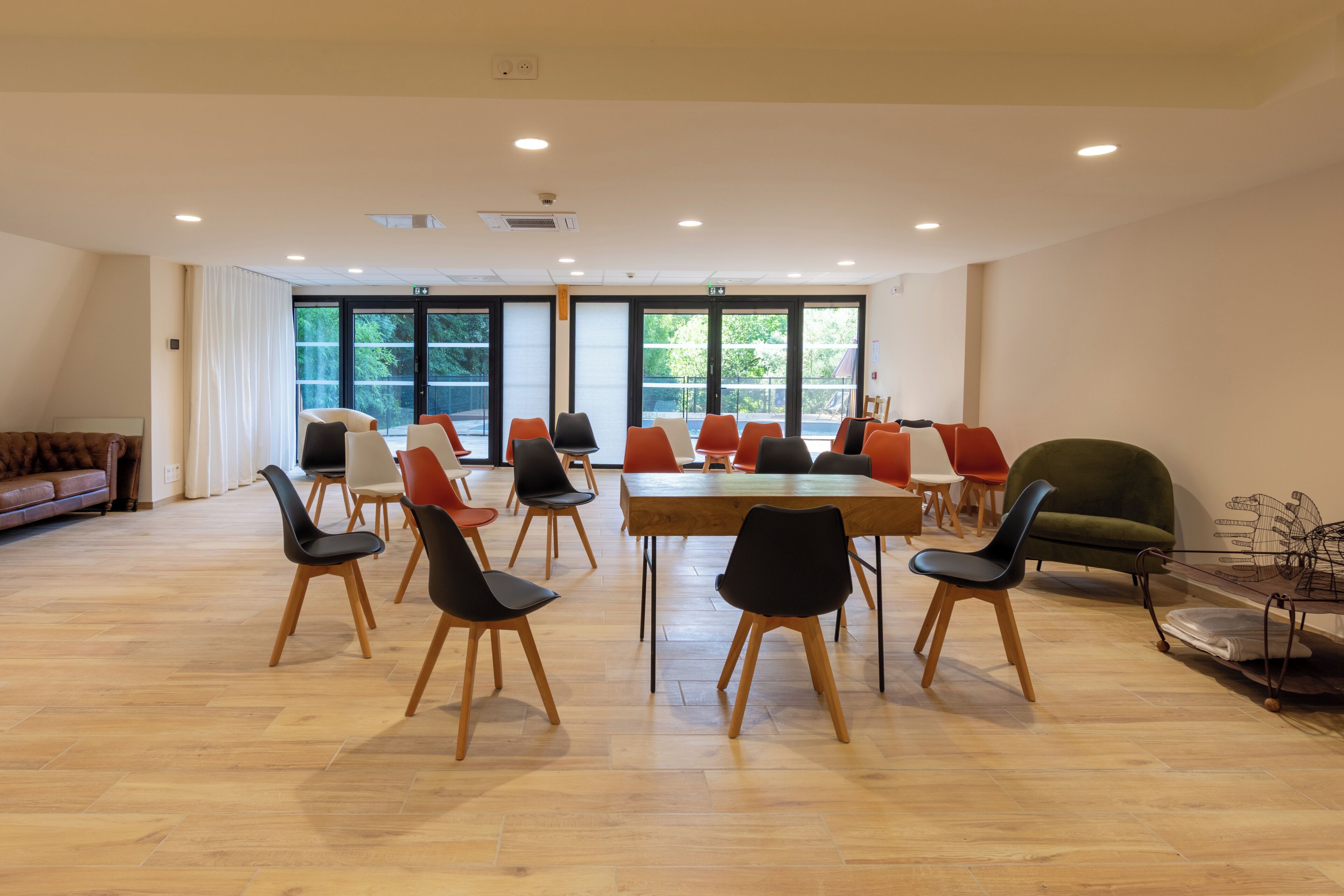 A spacious room with a large table surrounded by chairs, large windows, and a sofa.