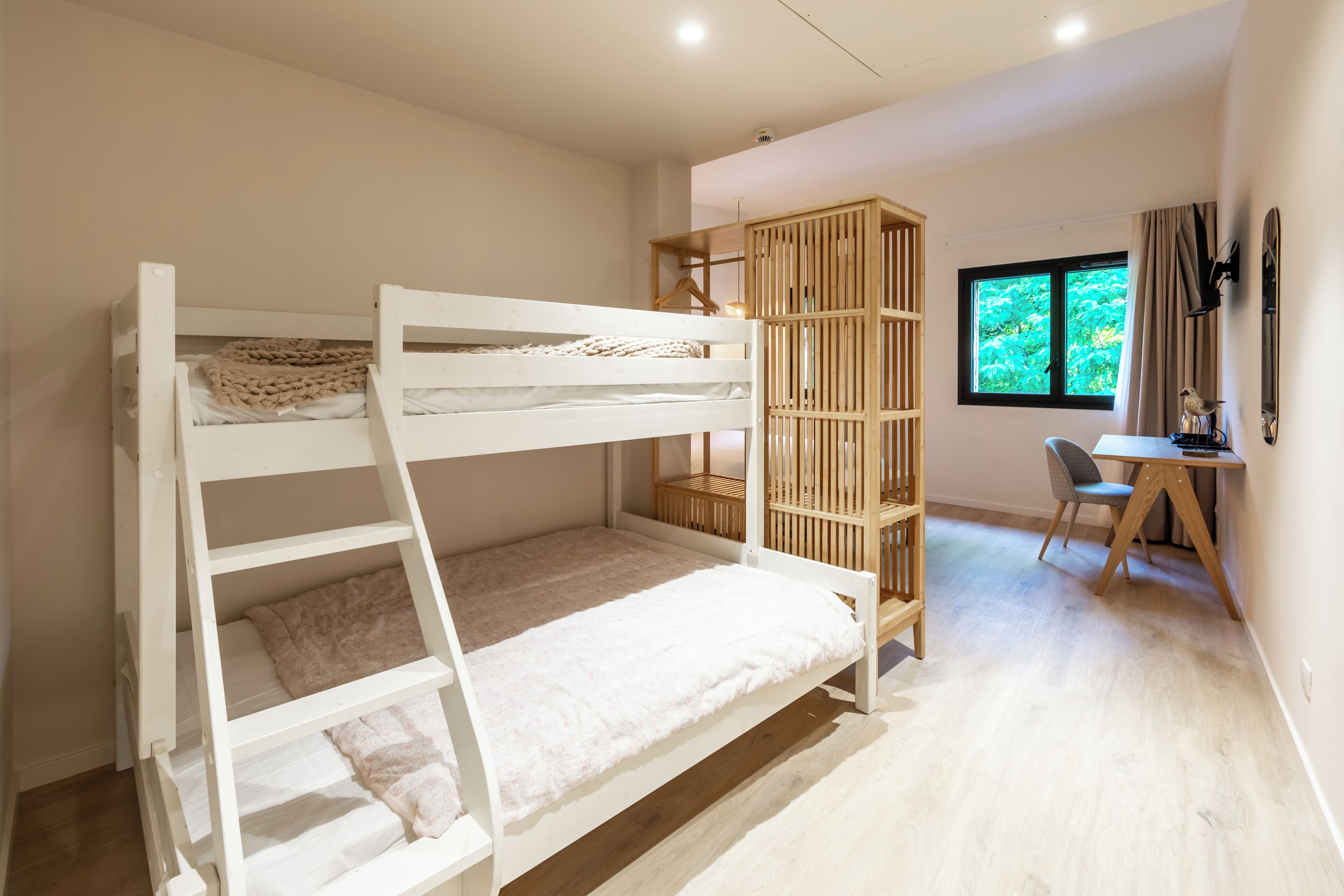 Una cama litera con escalera de madera, un escritorio con silla y una ventana con cortinas.