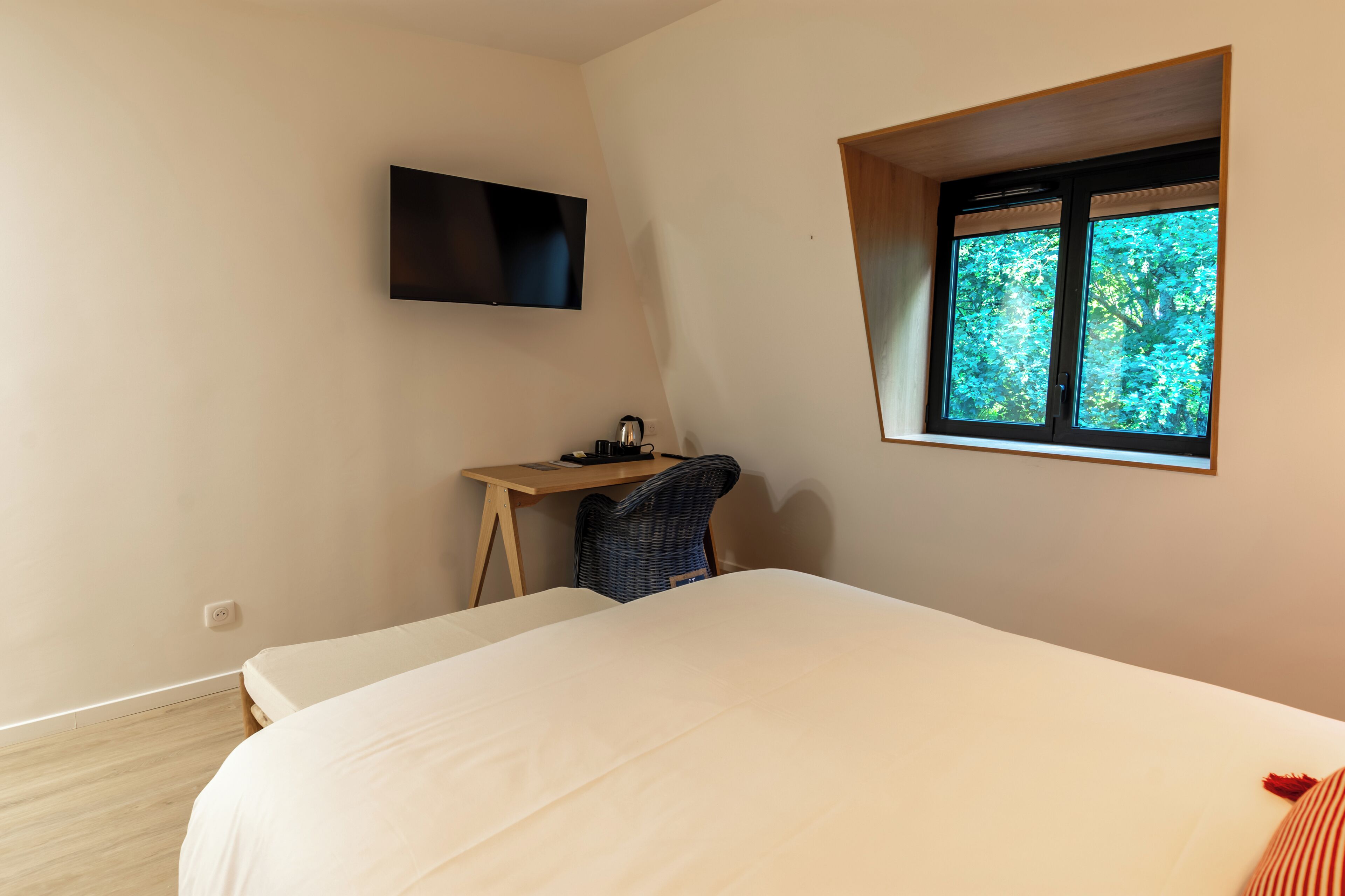 Un dormitorio con cama, escritorio, silla, televisión y ventana con vistas a árboles.