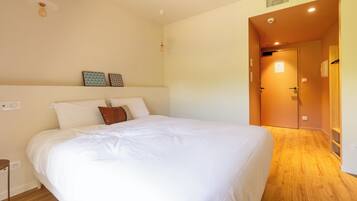 Une chambre avec un grand lit, un plancher en bois, une porte donnant sur une autre pièce et un luminaire au plafond.