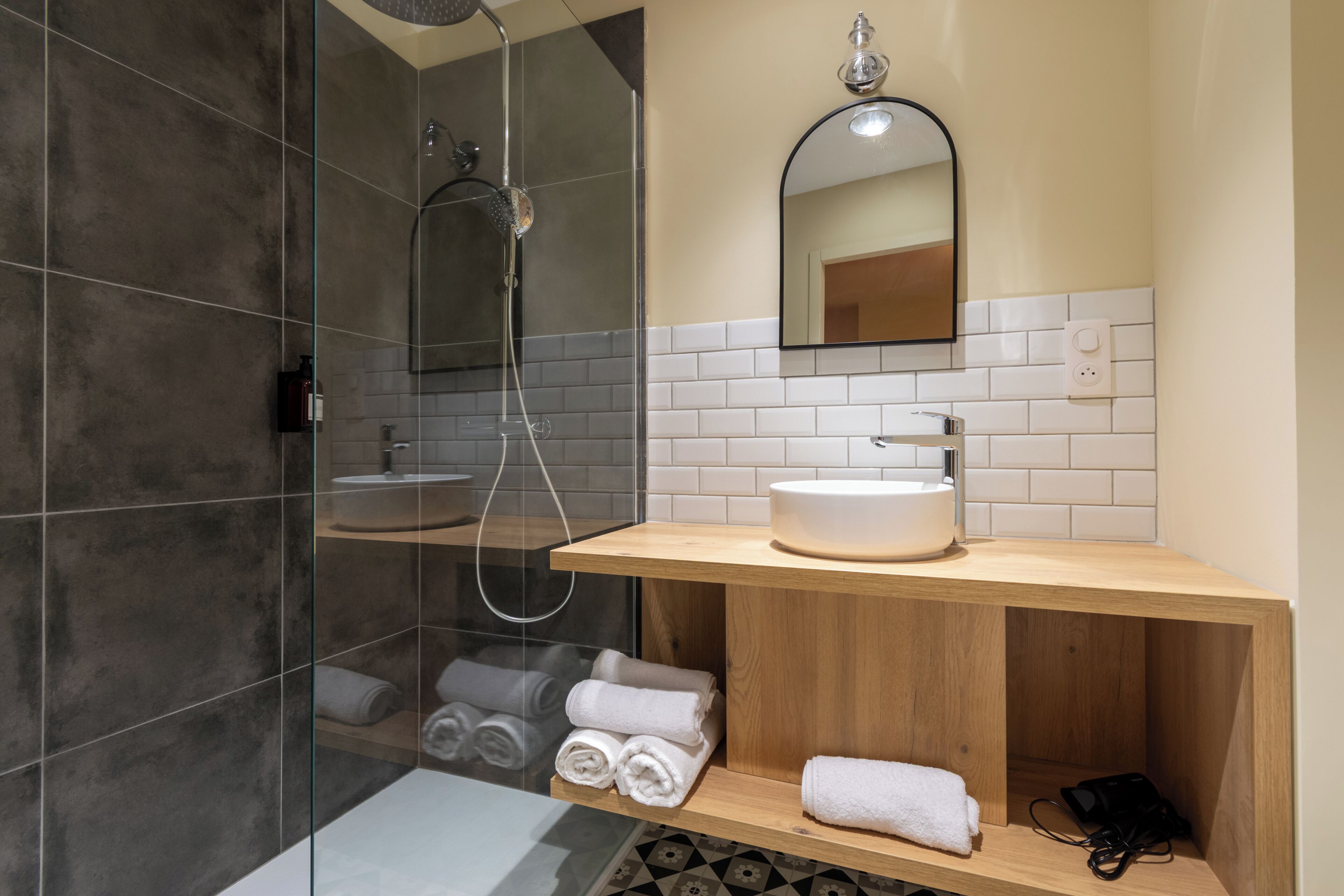 Un baño moderno con ducha envuelta en vidrio, tocador de madera con lavamanos y toallas dobladas cuidadosamente.