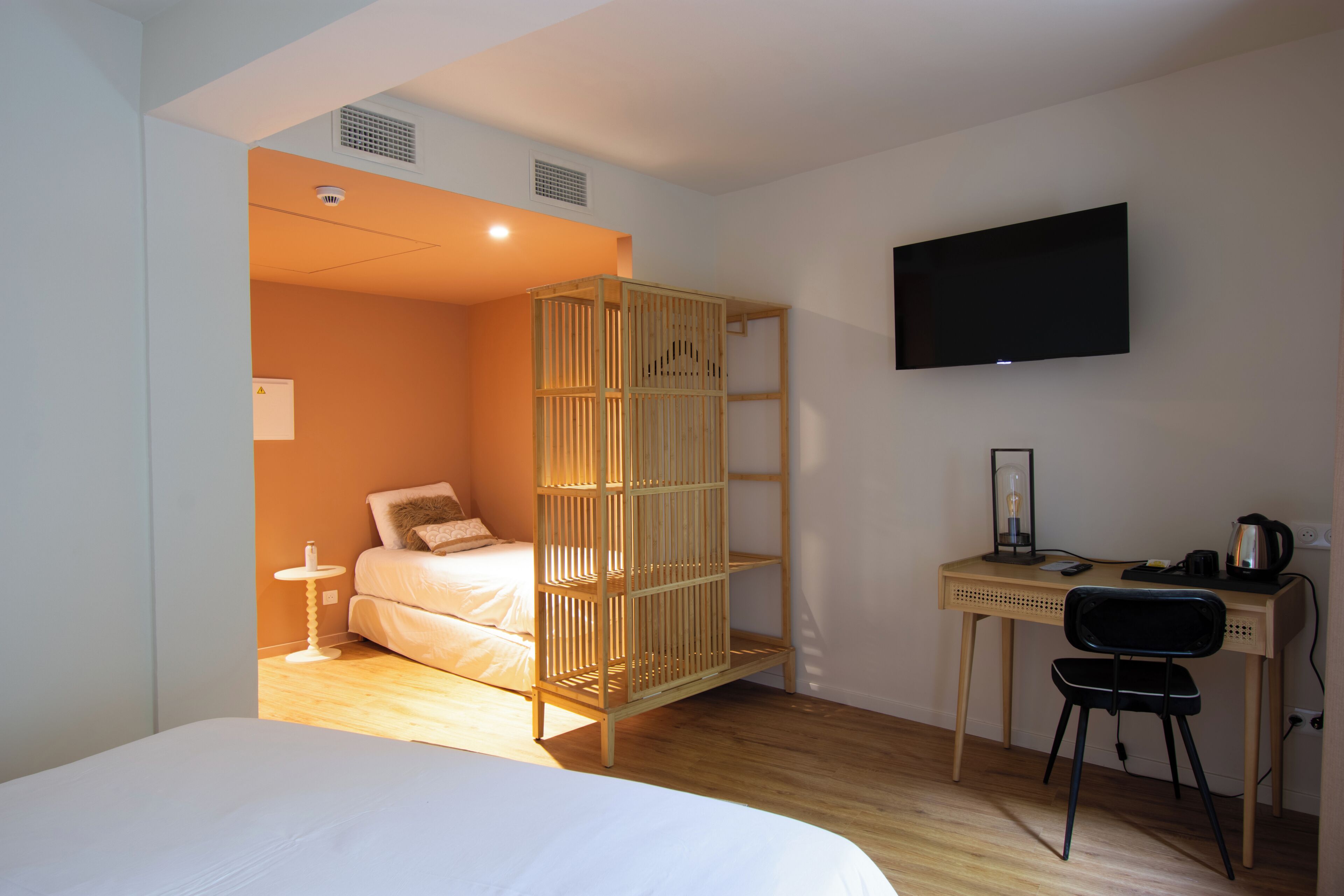A room with a bed, a desk with a chair, a television, and a wooden partition.