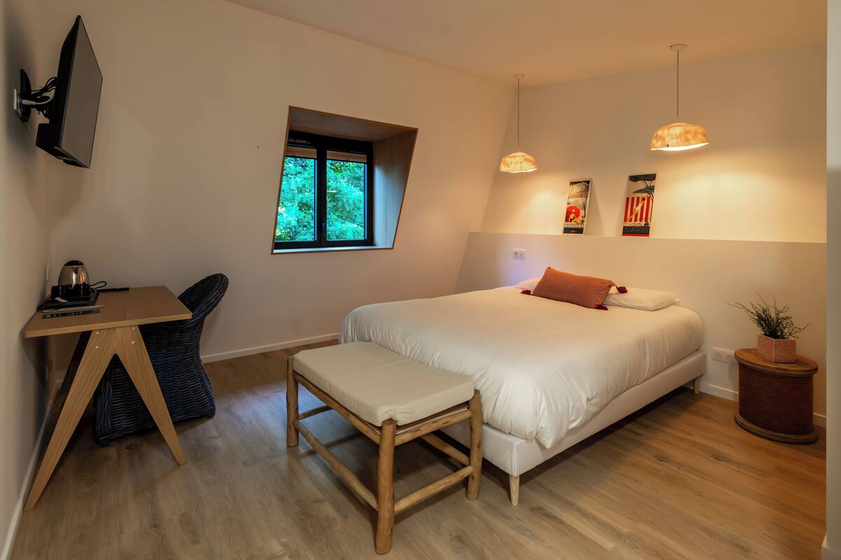 Une chambre à coucher avec un lit, un bureau, une chaise, une fenêtre et une plante en pot.