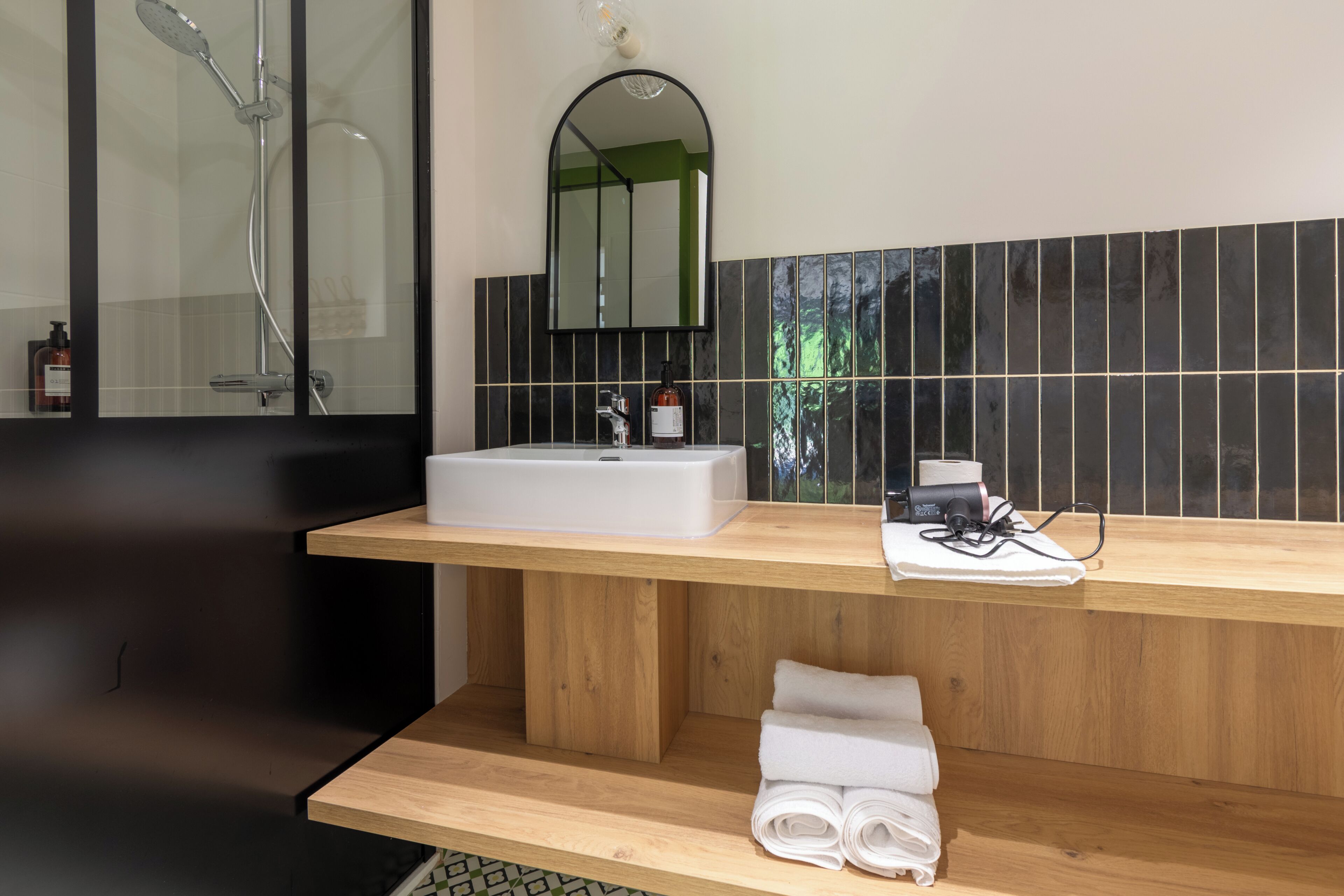 A modern bathroom with a wooden vanity, a white sink, a mirror, and a shower.