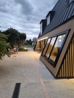 Un edificio moderno con grandes ventanales, camino de grava y mobiliario exterior.