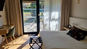 Une chambre d’hôtel avec un lit, un bureau, une chaise, une petite table avec une lampe, et une vue sur l’extérieur à travers une porte vitrée.