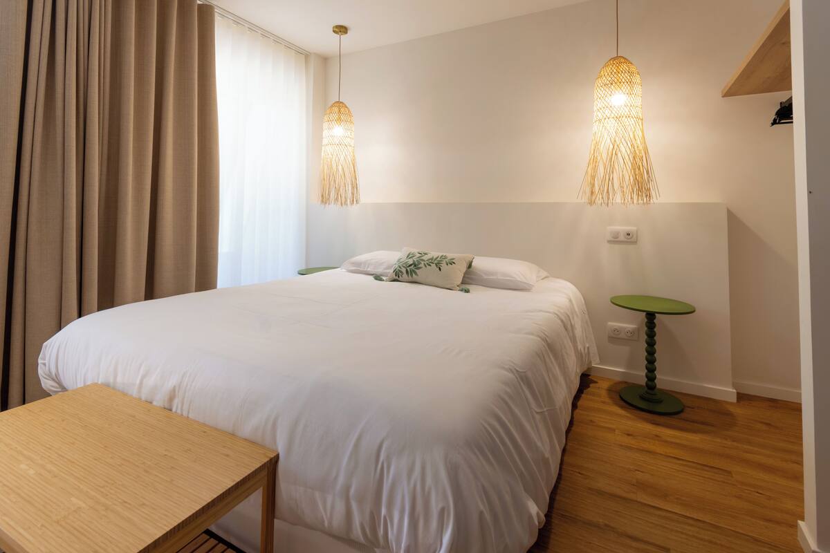 Une chambre à coucher comprenant un lit, une table de chevet, un luminaire suspendu et une petite table.