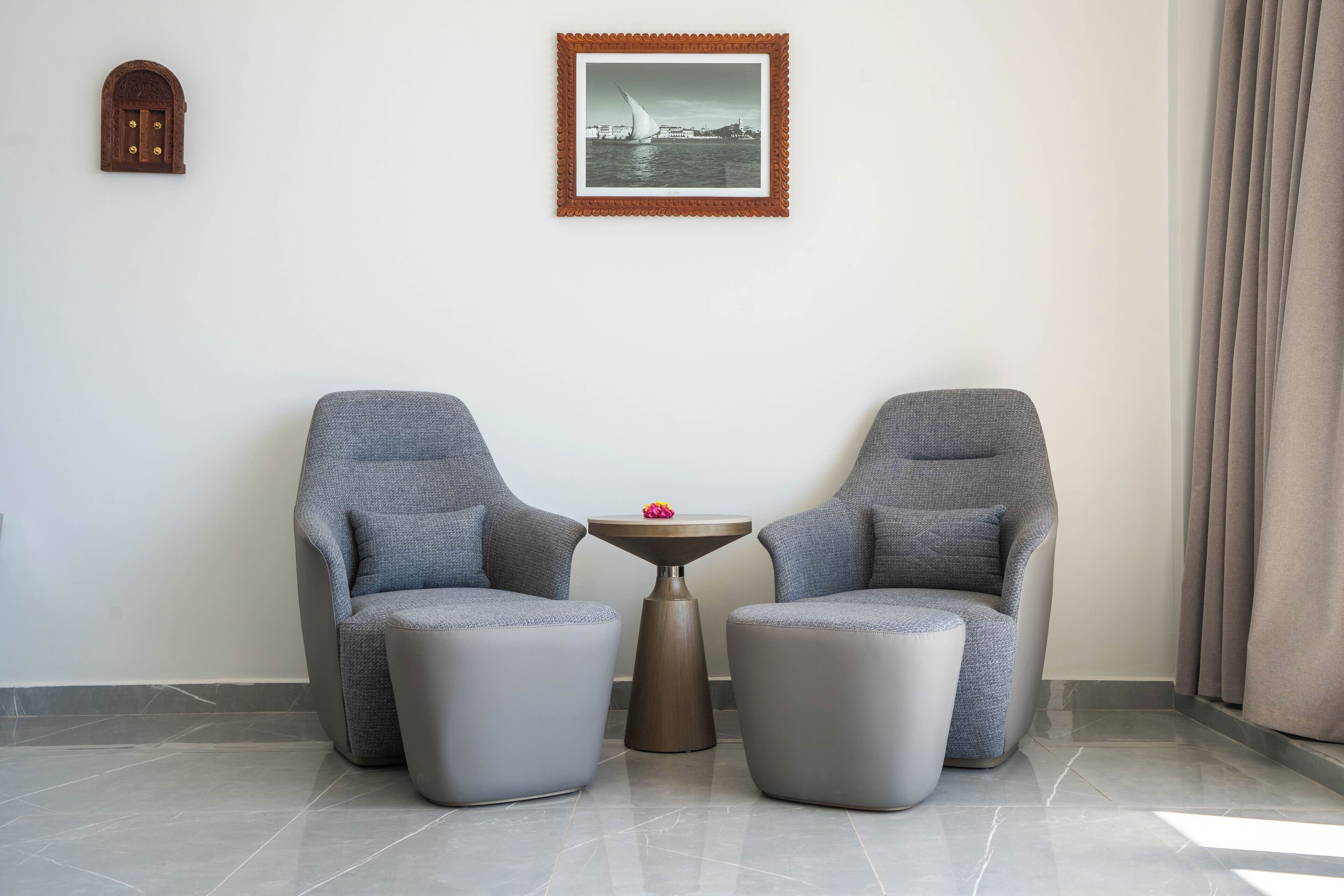 Una habitación con dos sillones grises, una pequeña mesa redonda con una flor, y un cuadro enmarcado en la pared.