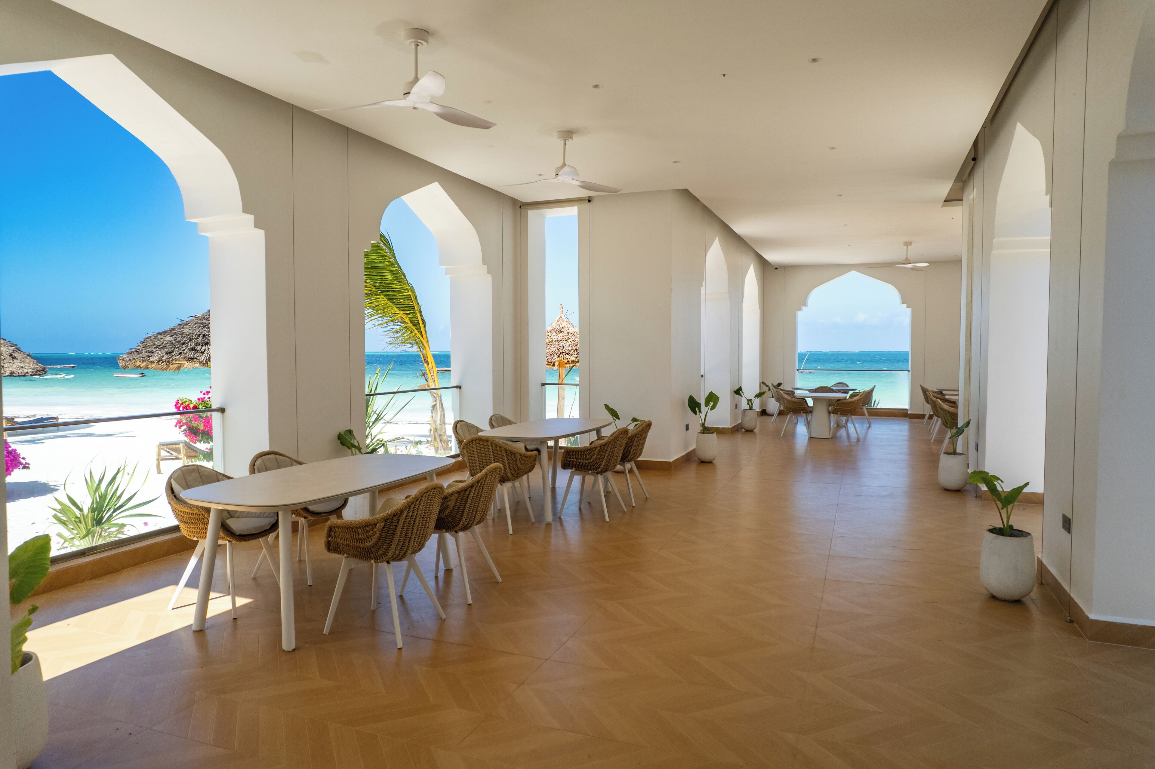 Un'ampia area interna con un tavolo grande e sedie, una ventola a soffitto e vista sull'oceano attraverso ampie finestre.