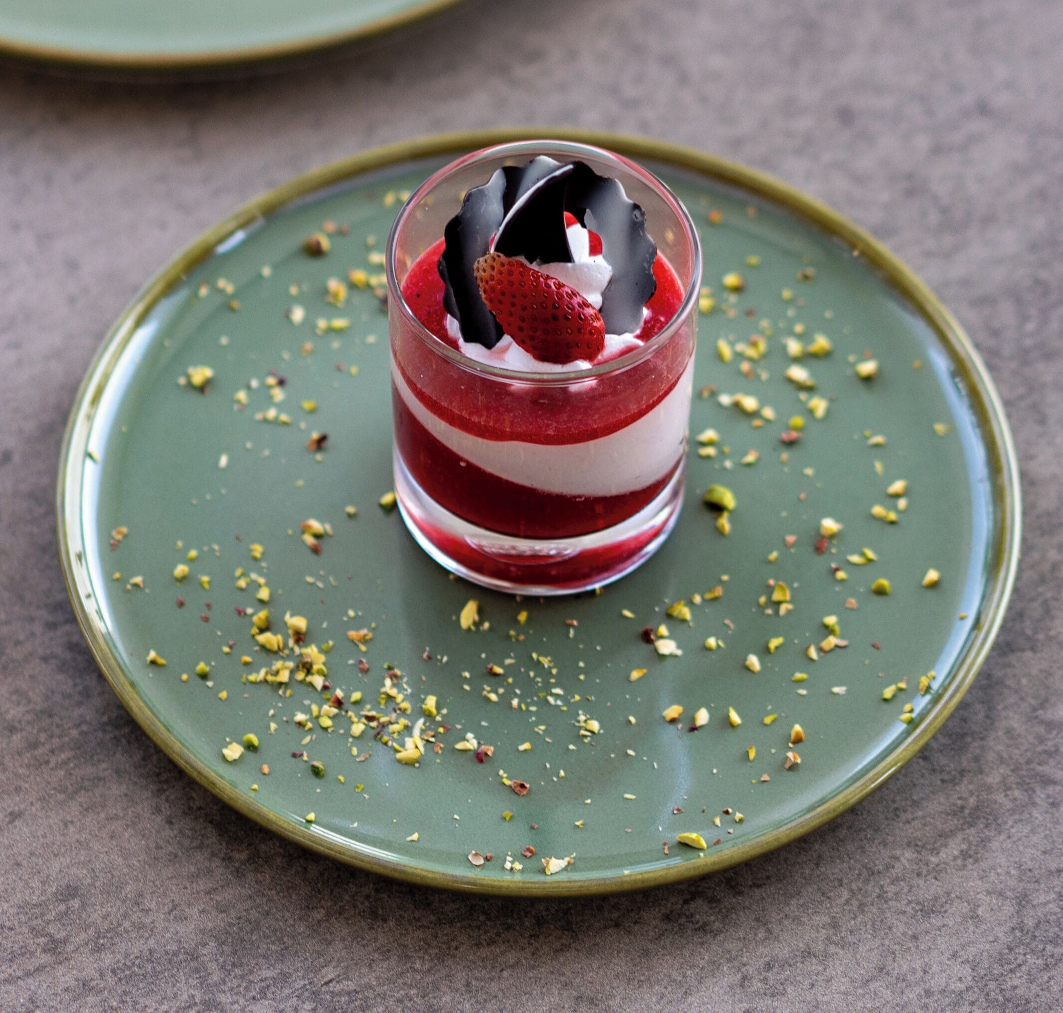A dessert with layers and a strawberry on a green plate with scattered nuts.