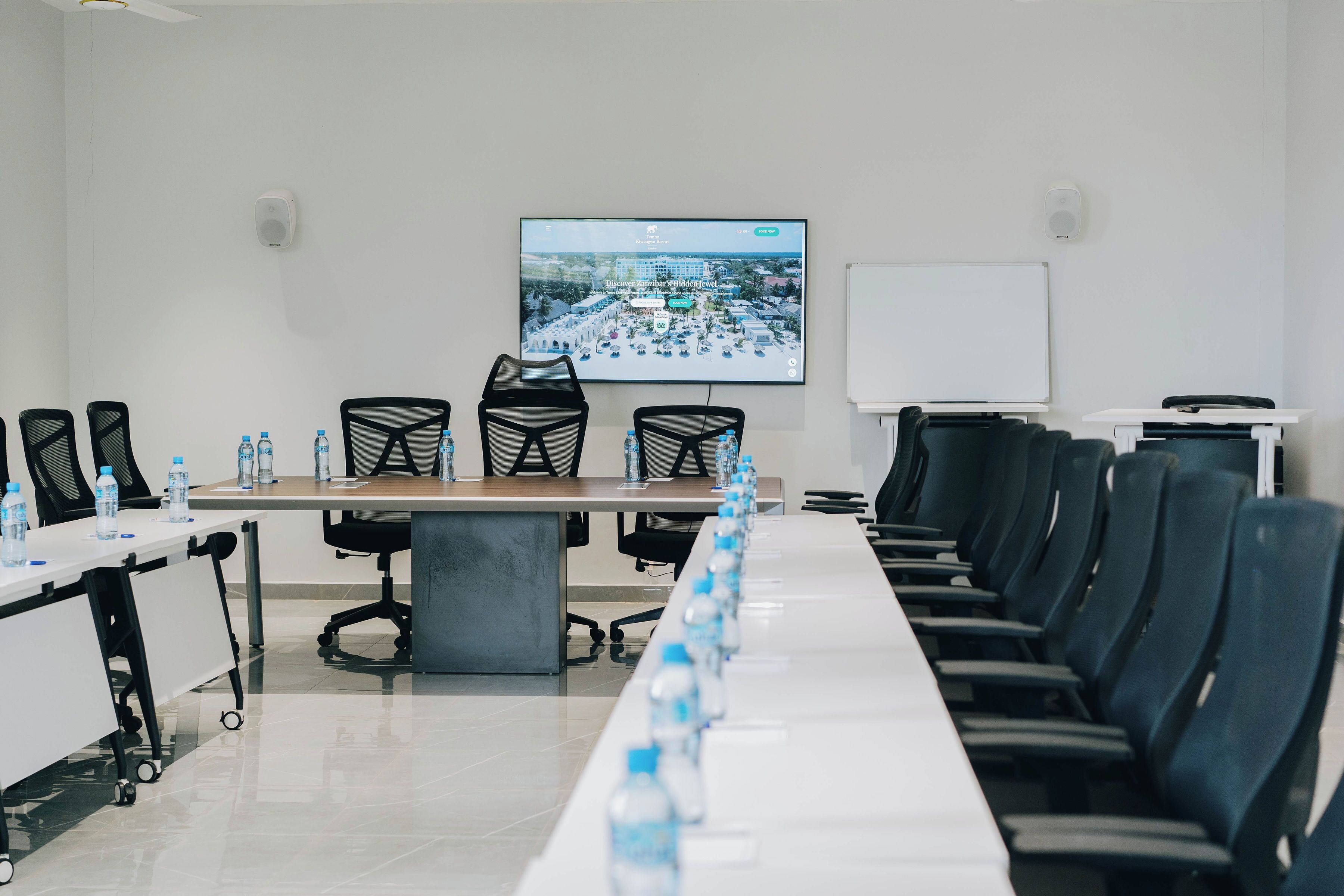 A conference room with a long table, chairs, a projector screen, and a whiteboard.