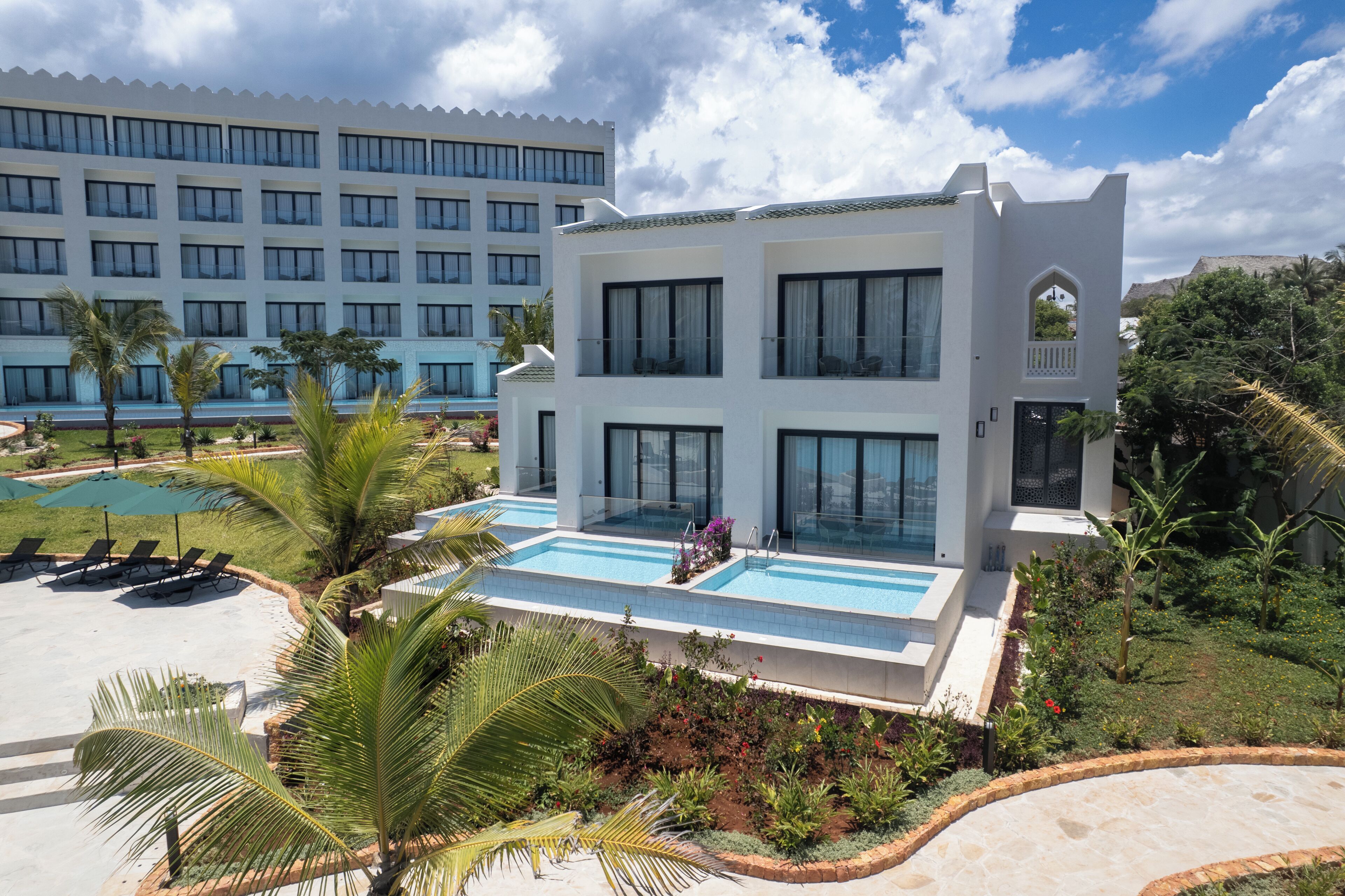 A modern hotel with a pool, lounge chairs, and a landscaped garden.