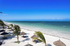 Uma praia com areia branca, palmeiras e guarda-sóis de palha.
