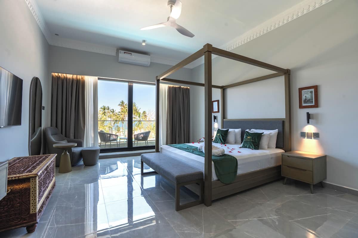 Een moderne hotelkamer met een hemelbed, een balkon met uitzicht, een zithoek met een tafel en een decoratieve kist.
