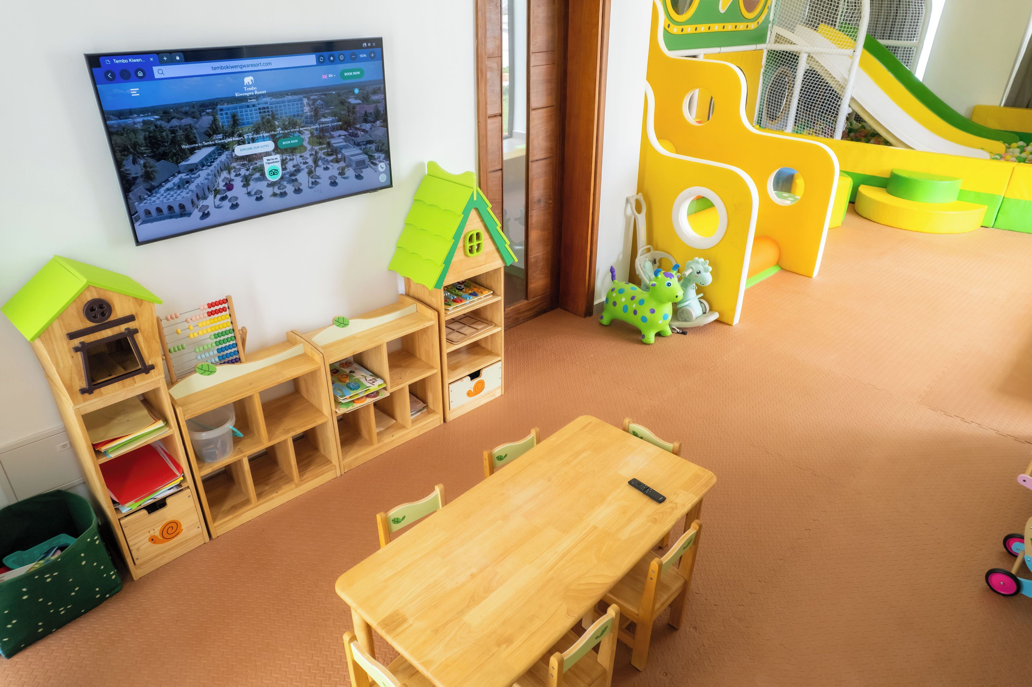 A children's play area with a slide, a playhouse, and a TV mounted on the wall.