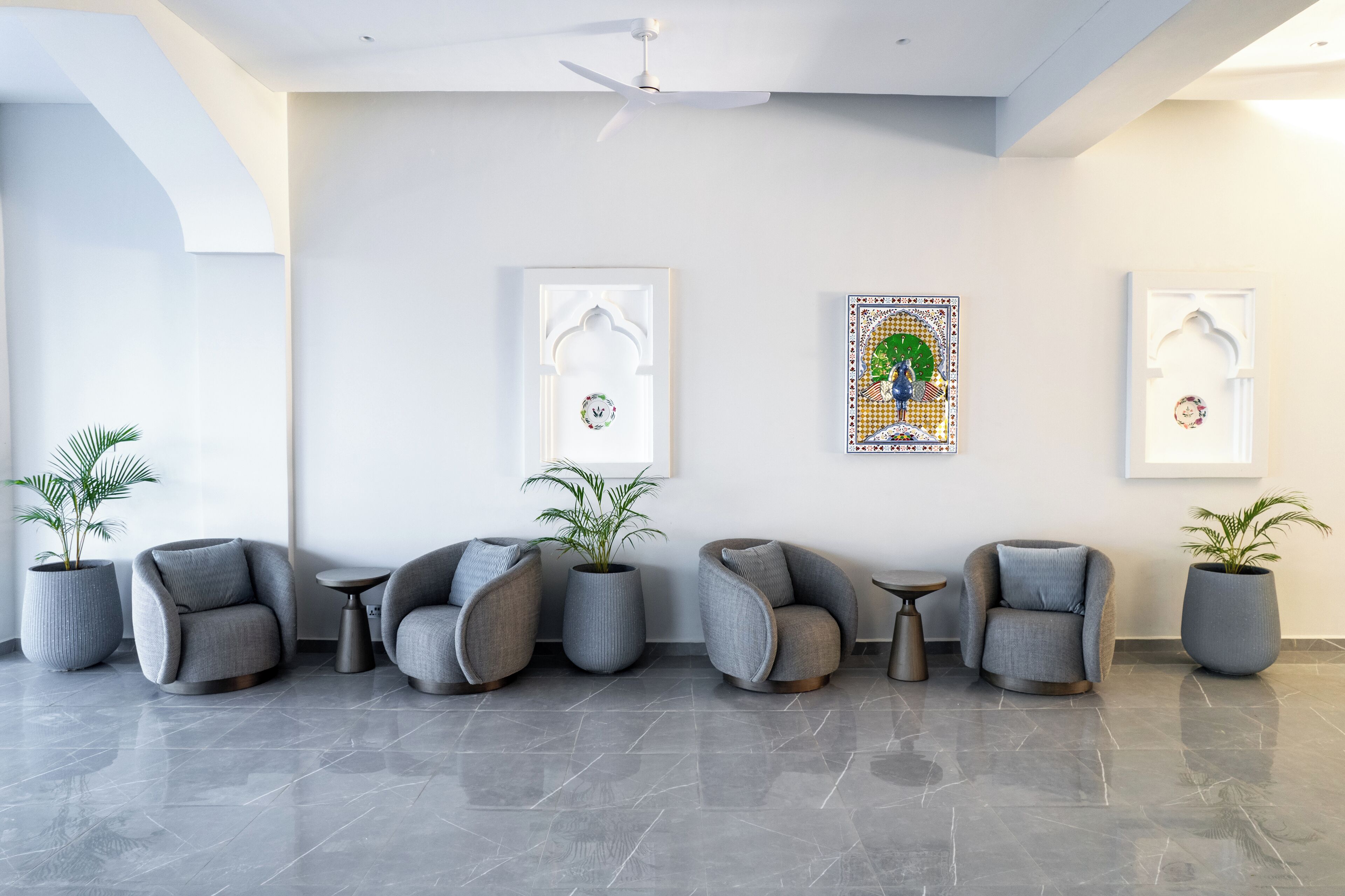 A modern lobby with grey upholstered chairs, potted plants, and framed artwork on the walls.