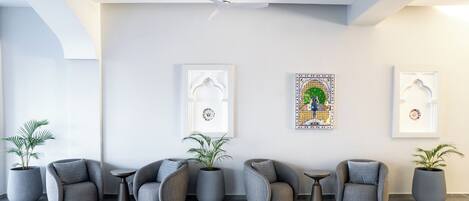 A modern lobby with grey upholstered chairs, potted plants, and framed artwork on the walls.